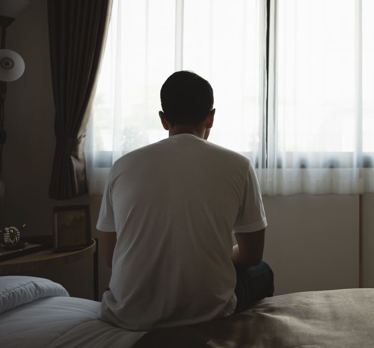 Man sitting alone on a bed facing a window – online psychiatry in Fresno, CA